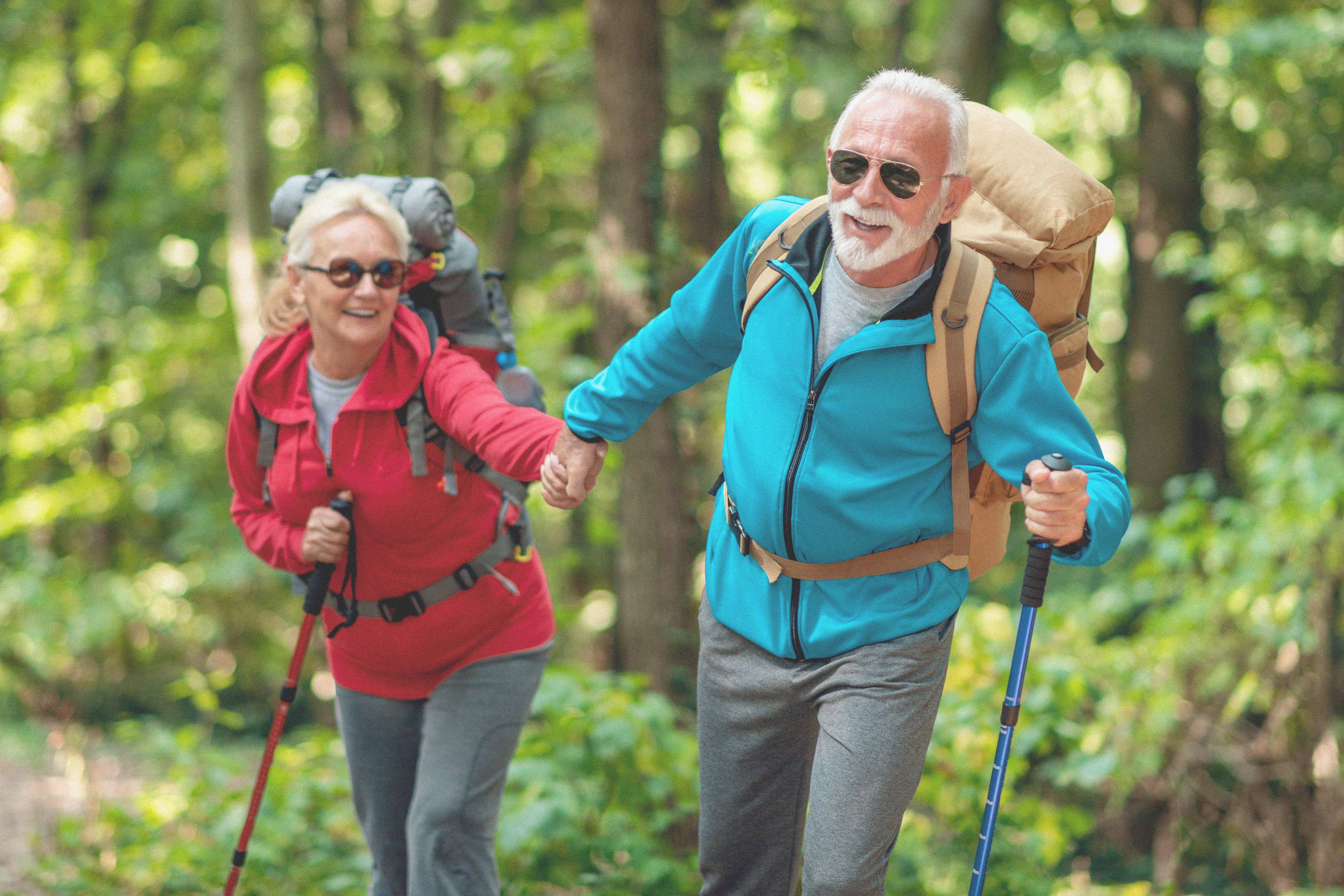 Older couple hiking in the woods, smiling and holding hands